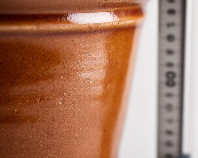 Detailaufnahme einer glasierten Terracotta-Planter-Oberfläche neben einem Massband in einem sauberen Werkstattbereich